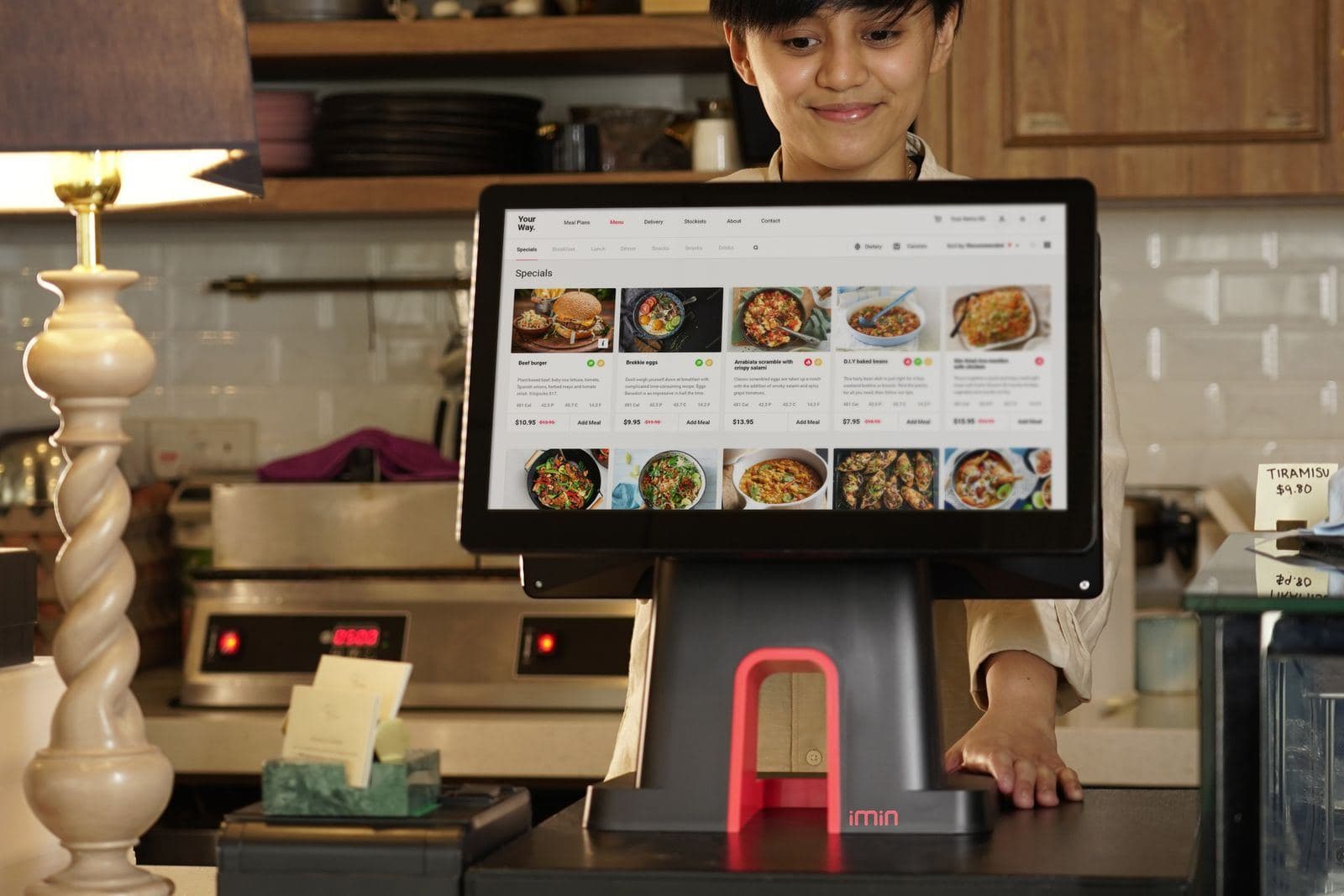 Encargada de un restaurante usando una pantalla de punto de venta en el mostrador.